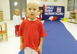 Ernest ubrany na biało czerwono pozuje podczas "Pokazu mody patriotycznej" na granatowym dywanie.